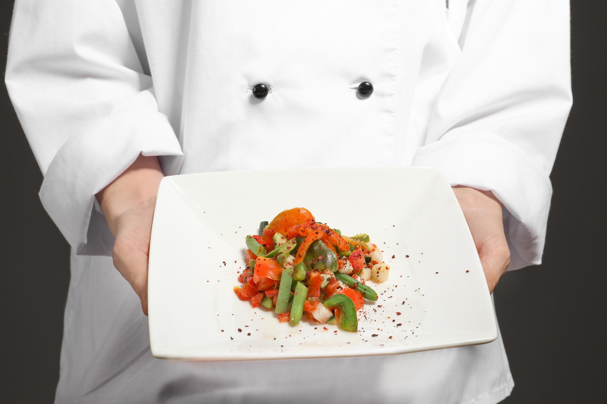 Chef demonstrating a plated dish on a warm wooden table